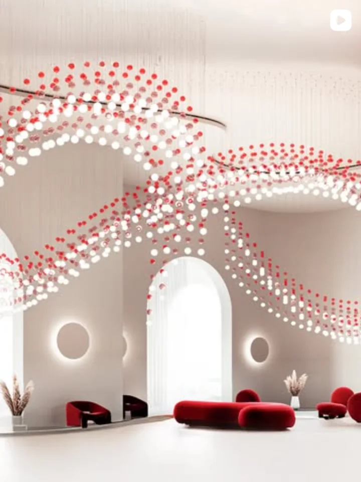 An Illuminatics Instagram post: a sculptural chandelier of red and white glass spheres sweeping over a white lobby with red seating.