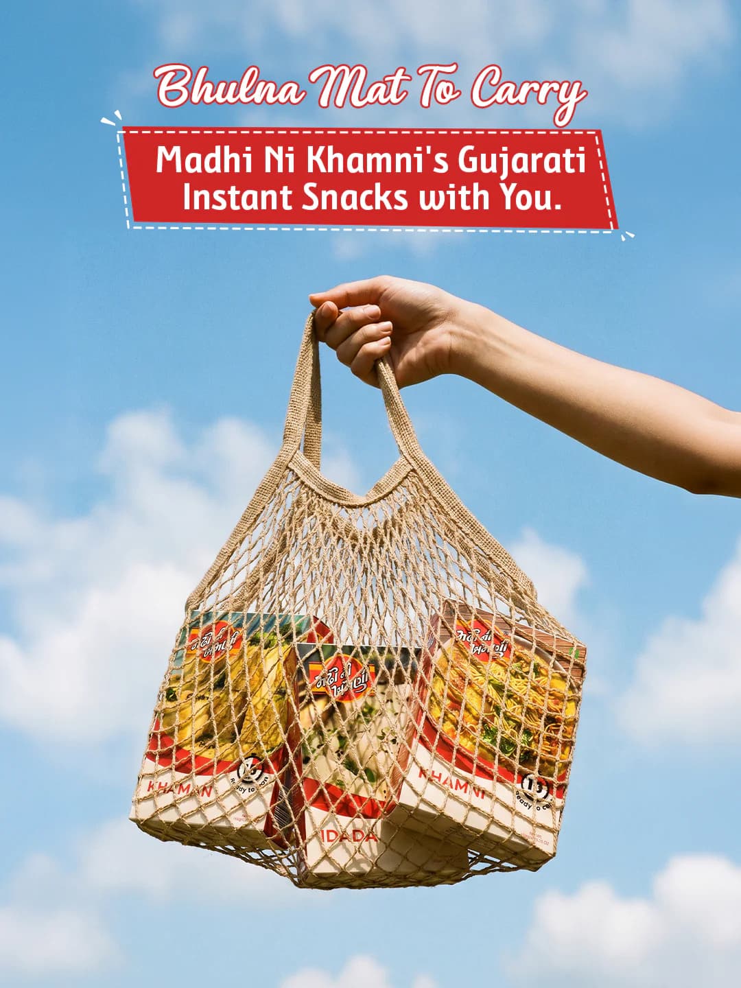 An MNK post, Bhulna mat to carry: a hand holds up a string bag of MNK snack boxes against a blue sky.